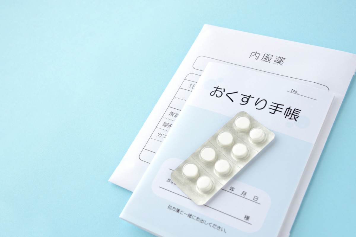薬袋の上に重なっているお薬手帳と錠剤の薬