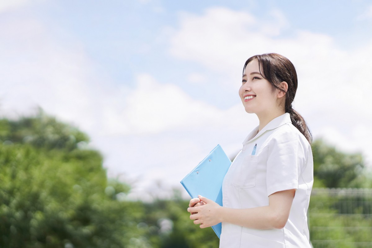 青い空を背景に手に青いファイルを持った笑顔の女性看護師