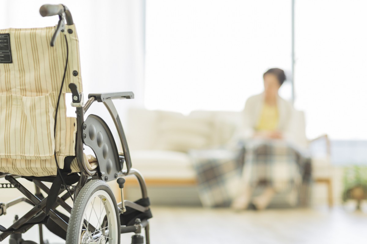 病室に置かれている車椅子と、ソファに座る高齢の女性